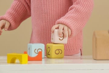 mani dinbambina con maglione rosa che gioca su un baco con dei cubi con le lettere